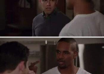 Two people having a conversation indoors; one man is wearing a plain t-shirt