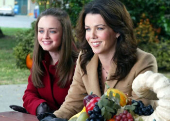 Rory and Lorelai Gilmore sit at a picnic bench smiling.