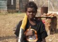 A young boy gives a thumbs up while holding a didgeridoo.