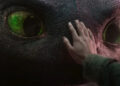 How To Train Your Dragon's Mason Thames places his hand on dragon Toothless' pebbled black face. .