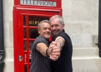 Stefan Dennis and Alan Fletcher dancing in front of a telephone booth.