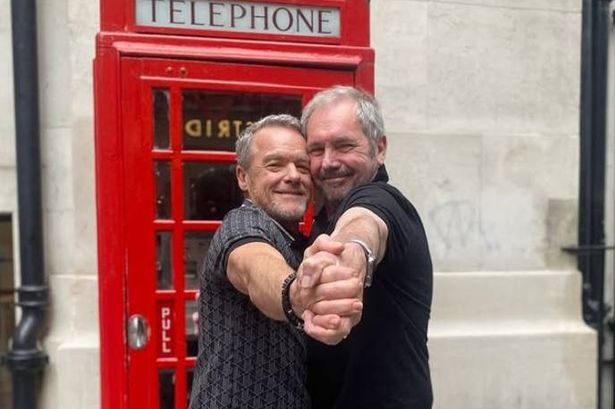 Stefan Dennis and Alan Fletcher dancing in front of a telephone booth.