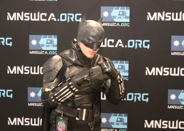 Person dressed as Batman strikes a pose with fists raised in front of banner reading "MNSWCA.org."