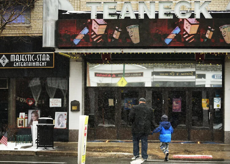 A man and child cross Cedar Lane in front of the movie theater as snow falls in Teaneck on Wednesday February 20, 2019.