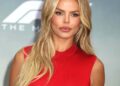 Brooks Nader poses at a red carpet event wearing a sleeveless red dress, her long blonde hair styled in loose waves.