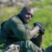 Adebayo Akinfenwa sat down wearing a harness and gloves at Hang Tough location.