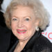Betty White smiles on the red carpet, wearing a black outfit with sparkling details and silver earrings