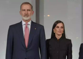 Felipe with a red tie and Letizia dressed in black serious looking to the side