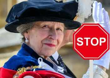 Elderly woman wearing an elegant hat and formal attire holding a red stop sign that says STOP
