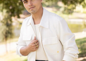 A man in a white jacket smiles in a park.