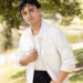 A man in a white jacket smiles in a park.