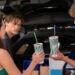 Three people holding smoothies near an open car trunk. Two are facing forward, one is looking back. They appear to be enjoying a casual moment