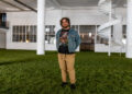 Ryan Patrick Hooper poses on the grass set inside the Boyer Campbell Building in Detroit for the Petrichor botanical art installation on May 30, 2024. (Photo credit: Tayler Simpson, WDET)