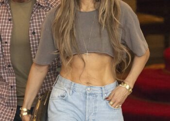 Jennifer Lopez wears a cropped gray T-shirt, light-wash wide-leg jeans, sunglasses and a New York Yankees cap while walking outside with a bodyguard.