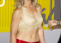 Jillian Michaels poses on the red carpet in a gold sequined crop top and red satin pants, holding a small clutch