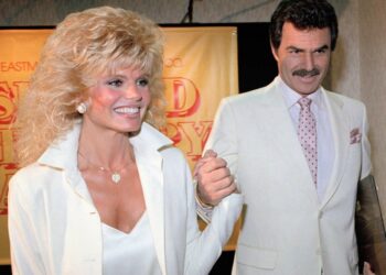 A man and woman wearing light coloured suits hold hands
