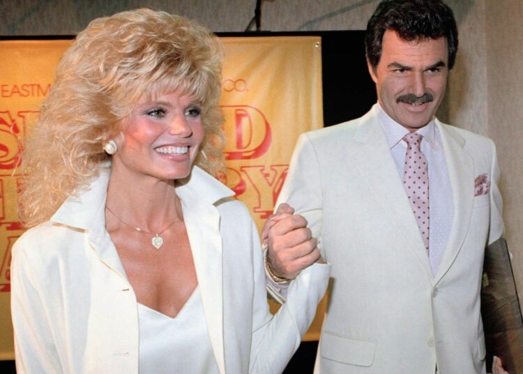 A man and woman wearing light coloured suits hold hands