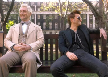 Michael Sheen and David Tennant smile on a park bench on Good Omens