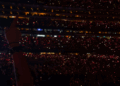 Crowd at a concert with lit-up phones emanating red light.