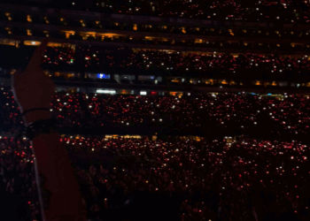 Crowd at a concert with lit-up phones emanating red light.