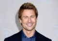 Glen Powell smiles on the red carpet in a navy jacket over a denim button-down shirt