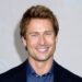 Glen Powell smiles on the red carpet in a navy jacket over a denim button-down shirt