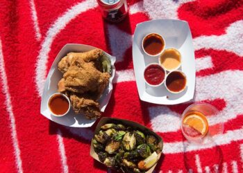 Fried chicken, Brussels sprouts, and sauces on a red picnic blanket.