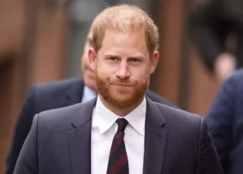 Prince Harry in a dark suit walks outdoors.