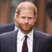 Prince Harry in a dark suit walks outdoors.