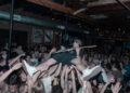 Zach Smith of The Espionage Act plays guitar while crowd surfing during a concert.