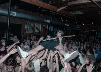 Zach Smith of The Espionage Act plays guitar while crowd surfing during a concert.