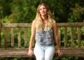 Emily Henry sits smiling on a bench in the park.