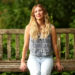 Emily Henry sits smiling on a bench in the park.