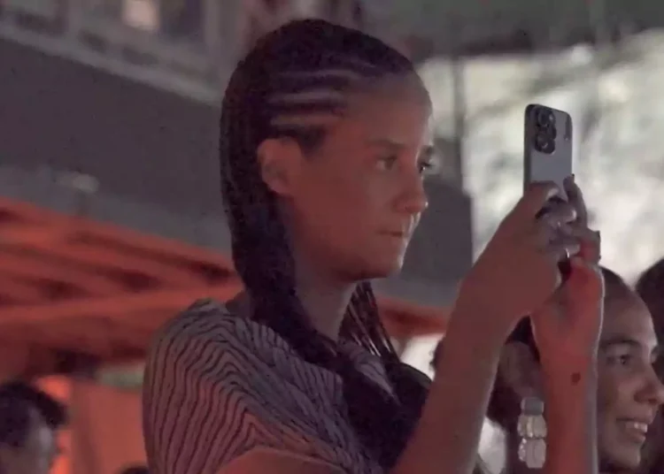 Young person with braids recording a video with their phone at an indoor event