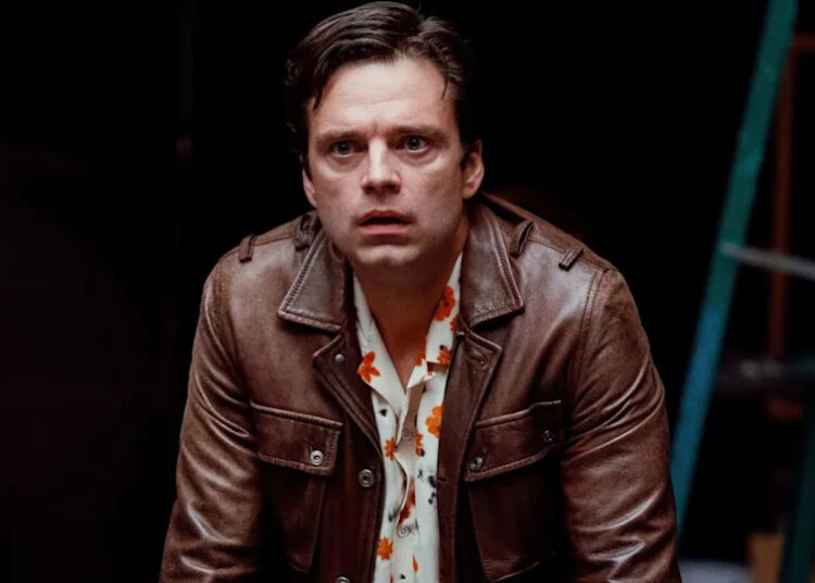 Sebastian Stan stands leaning over a table with a look of upset in A Different Man.