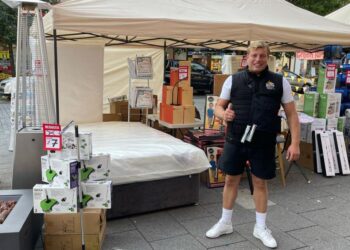 Man at a market stall selling bedding and cleaning supplies.