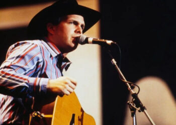 garth brooks singing on stage in black cowboy hat, striped shirt and jeans, holding a guitar