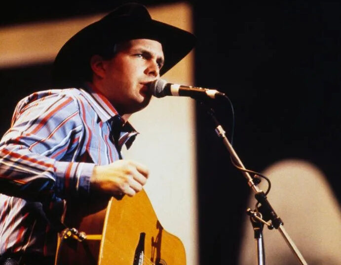 garth brooks singing on stage in black cowboy hat, striped shirt and jeans, holding a guitar