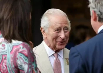 Older man with gray hair and a light-colored suit talking with two other people at a social event