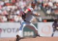 Gore in a solid grey jersey throwing a ball against the giants out of a black glove wearing a black and red ha