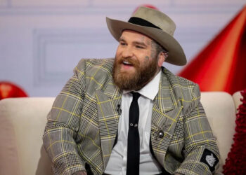 Teddy Swims smiles in a plaid suit jacket and hat.