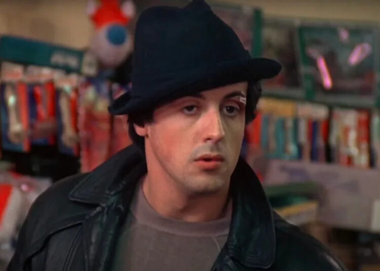 Sylvester Stallone's Rocky inside pet store wearing his black hat and black leather jacket.