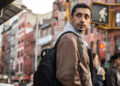 Riz Ahmed with a backpack near a crosswalk in Relay.