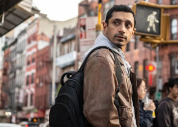 Riz Ahmed with a backpack near a crosswalk in Relay.