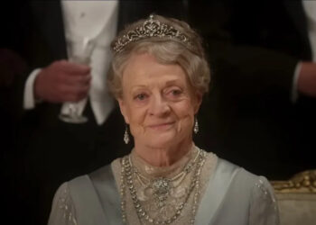 Dame Maggie Smith sits dressed in her finest smiling at a ball in Downton Abbey: The Movie.