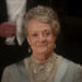 Dame Maggie Smith sits dressed in her finest smiling at a ball in Downton Abbey: The Movie.