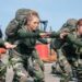 military personnel performing physical training exercises outdoors with backpacks