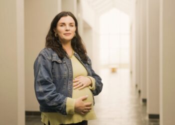 A woman cradling her baby bump as she smiles and looks ahead.