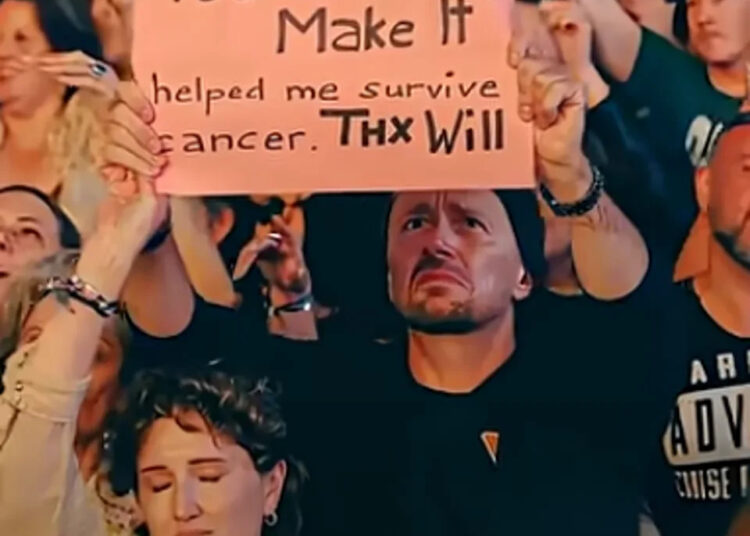 A woman's headband seems to go over the wrist of the woman in front, while her own hand morphs into the man holding up a sign (YouTube/Will Smith)