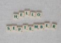 "Scrabble tiles spell 'Hello September' on a textured gray background."
